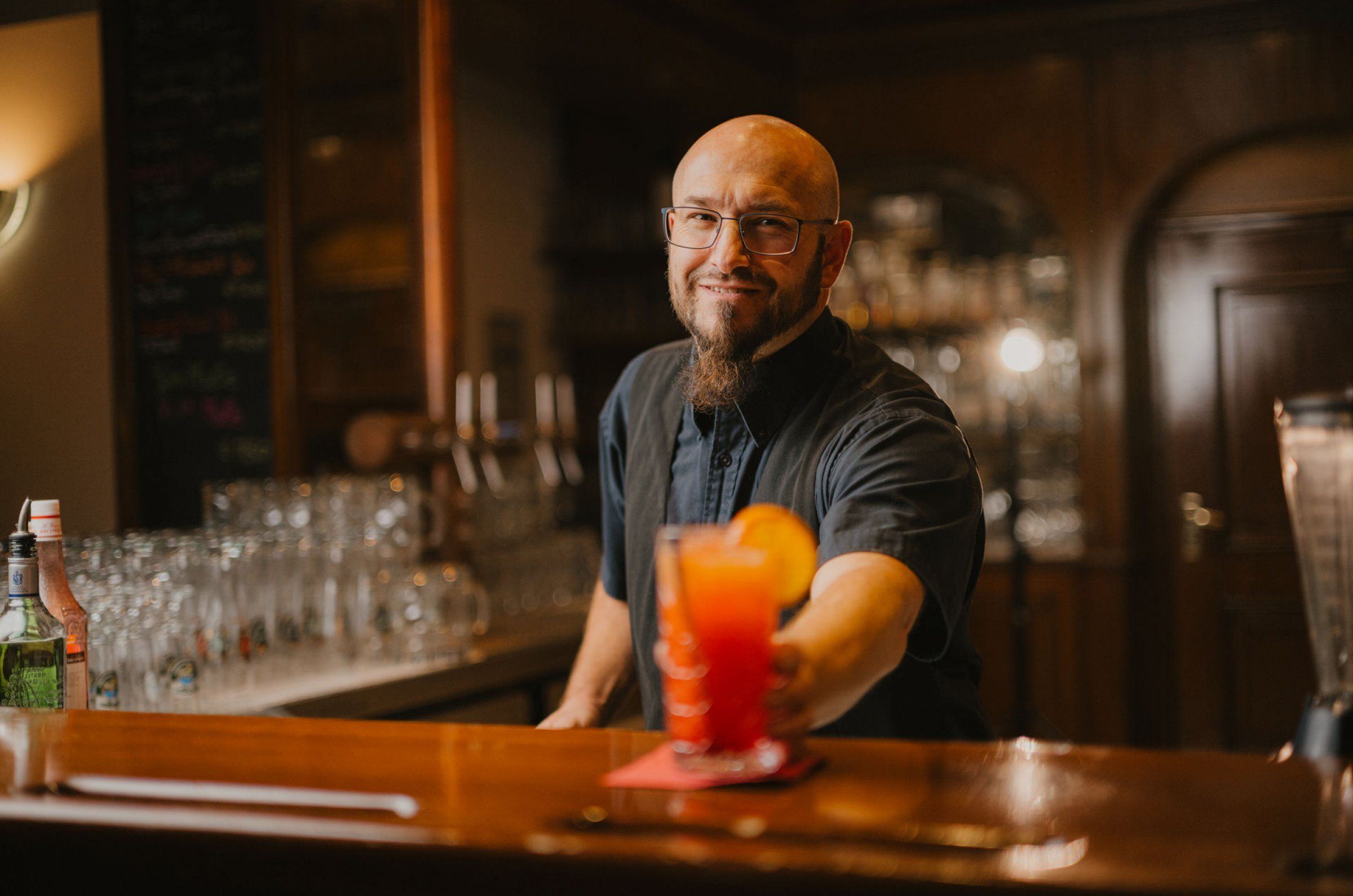 Barchef Alex reicht einen Cocktail über die Theke