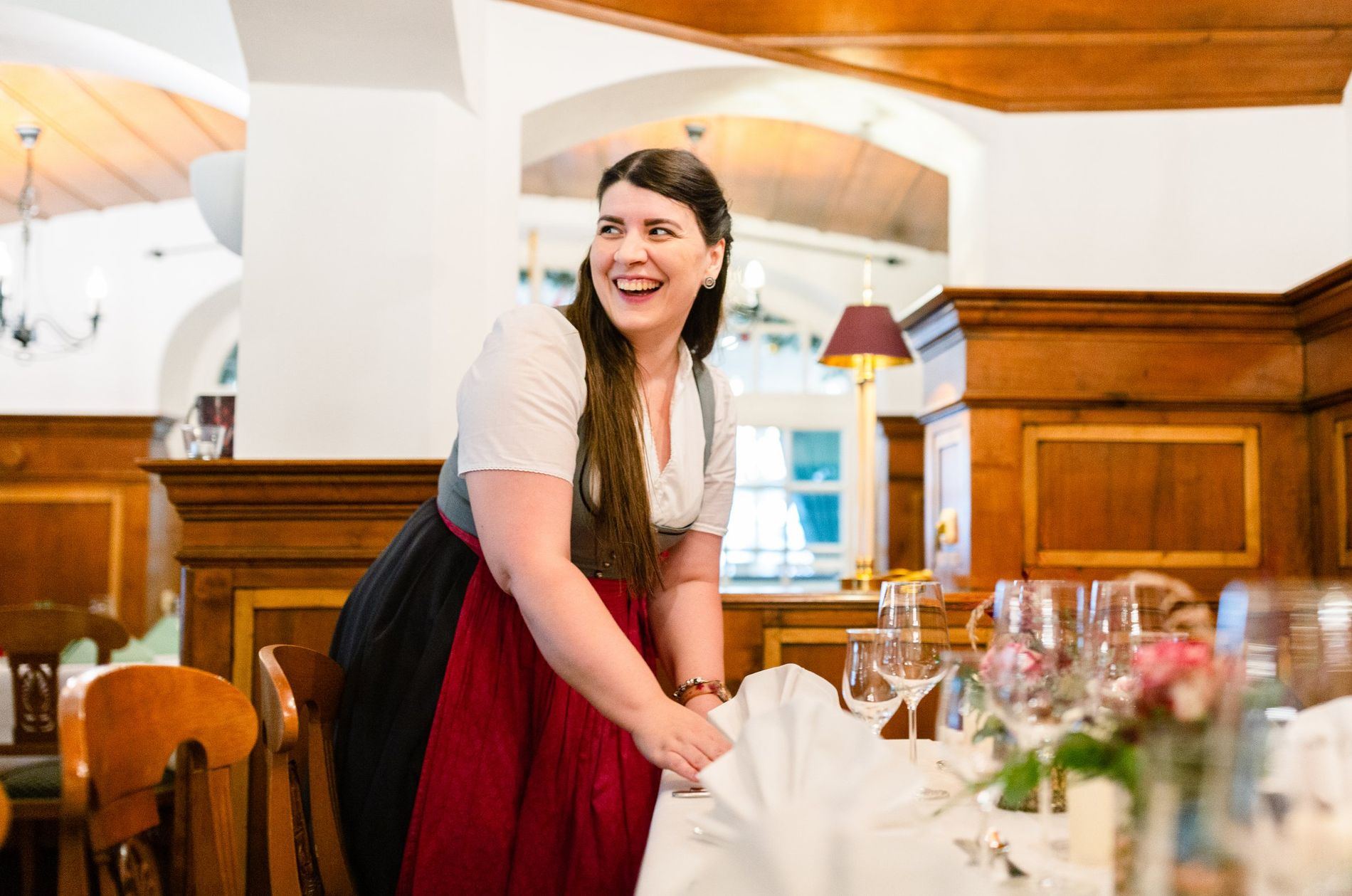 Gastgeberin in Tracht deckt lachend einen Tisch im Restaurant