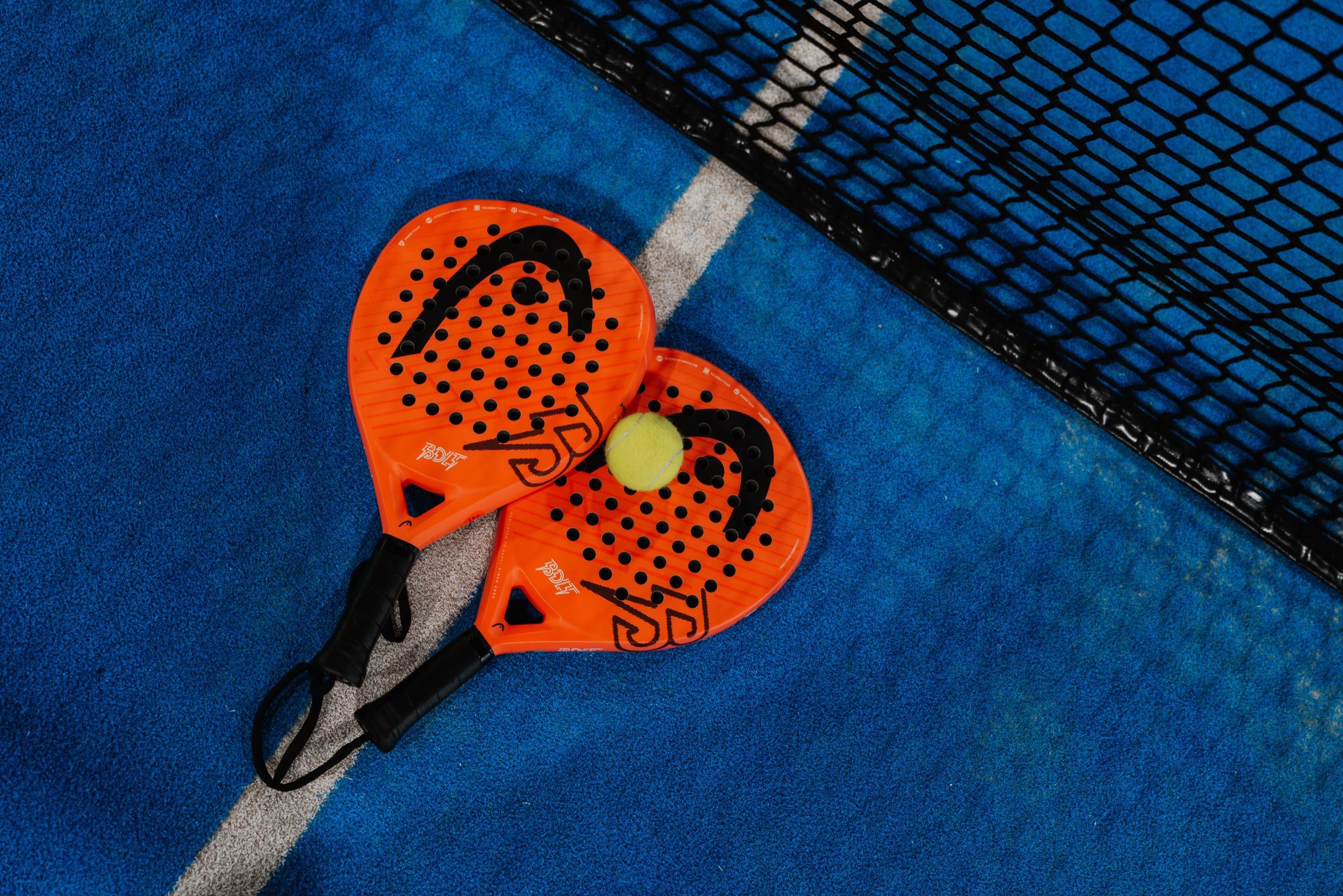 Two padel rackets and a ball at the net of an indoor padel court